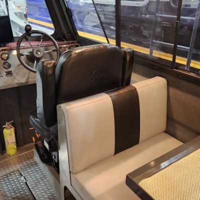 Inside a pilot boat cabin with a steering wheel, control panel, seating, and a table.