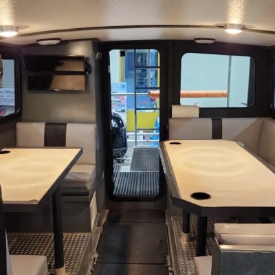 Interior of a boat cabin with tables, benches, wall photos, and windows.