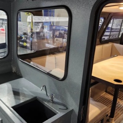 Interior of a boat showing a small kitchenette and a dining area with seating.
