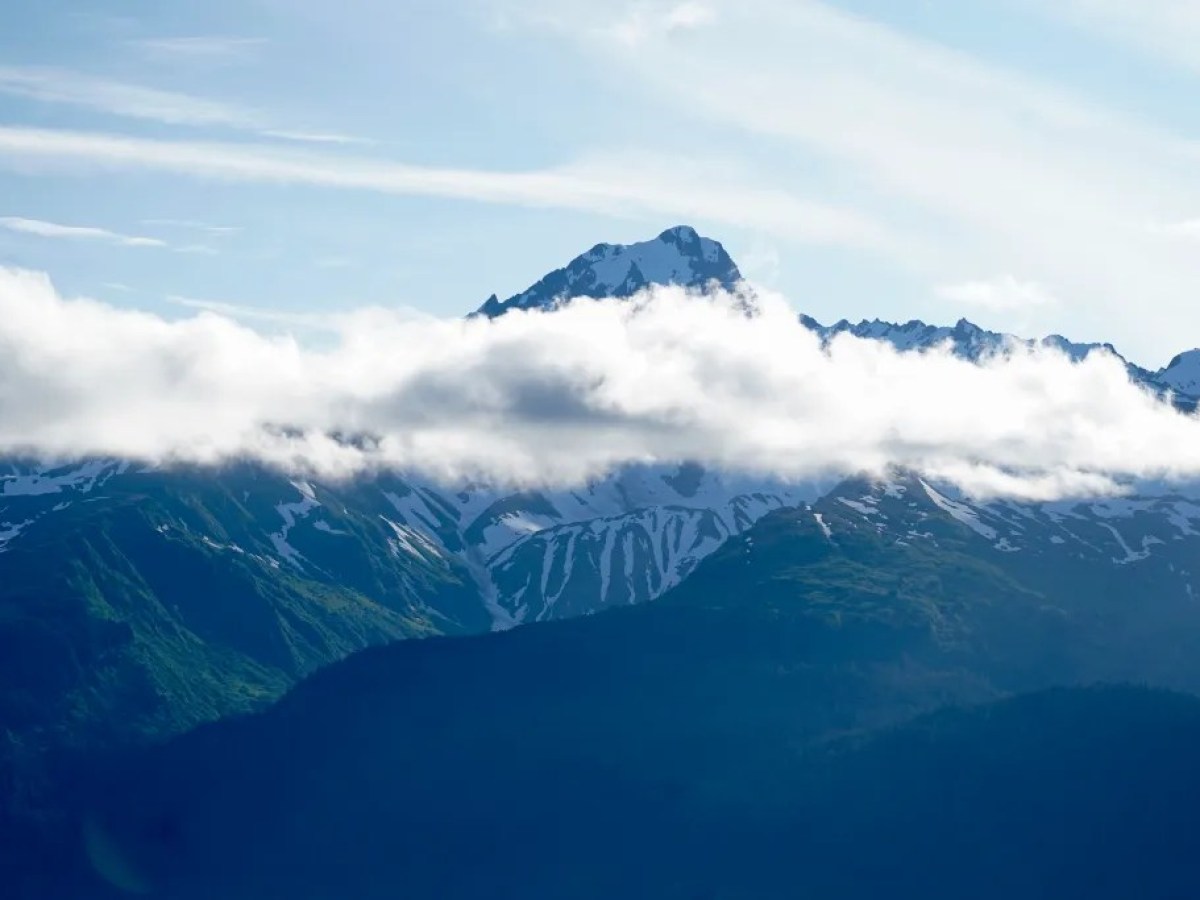 Snow-capped mountain peak partially obscured by a band of clouds.