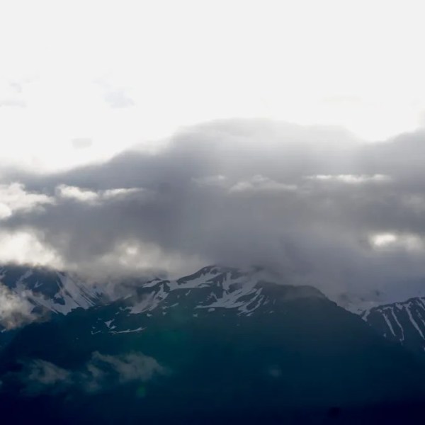 Snow-covered mountains partially obscured by dark clouds on a cloudy day.