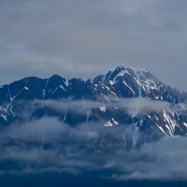Snow-capped mountain peak with patches of clouds and blue sky.
