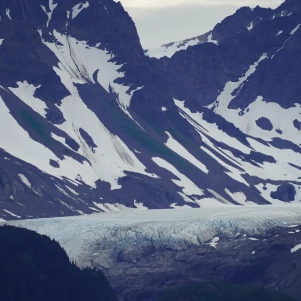 Snow-capped mountains with a glacier in the valley under a cloudy sky.