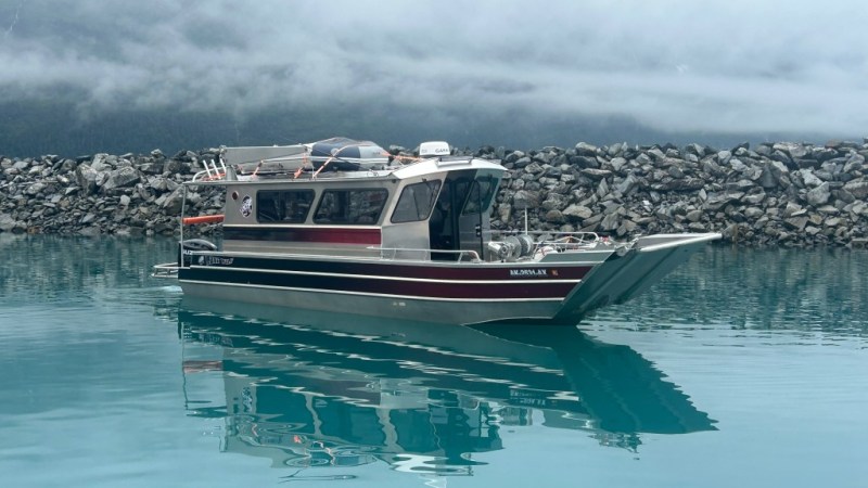 Boat with red and gray stripes on calm water, cloudy mountains in the background.