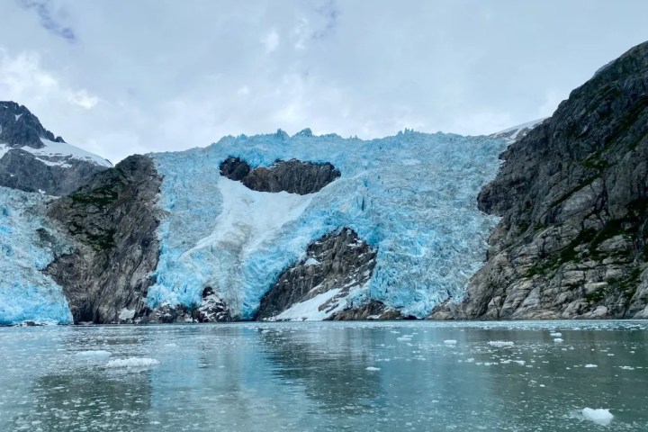 Blue glacier surrounded by rocky cliffs and a calm water surface.