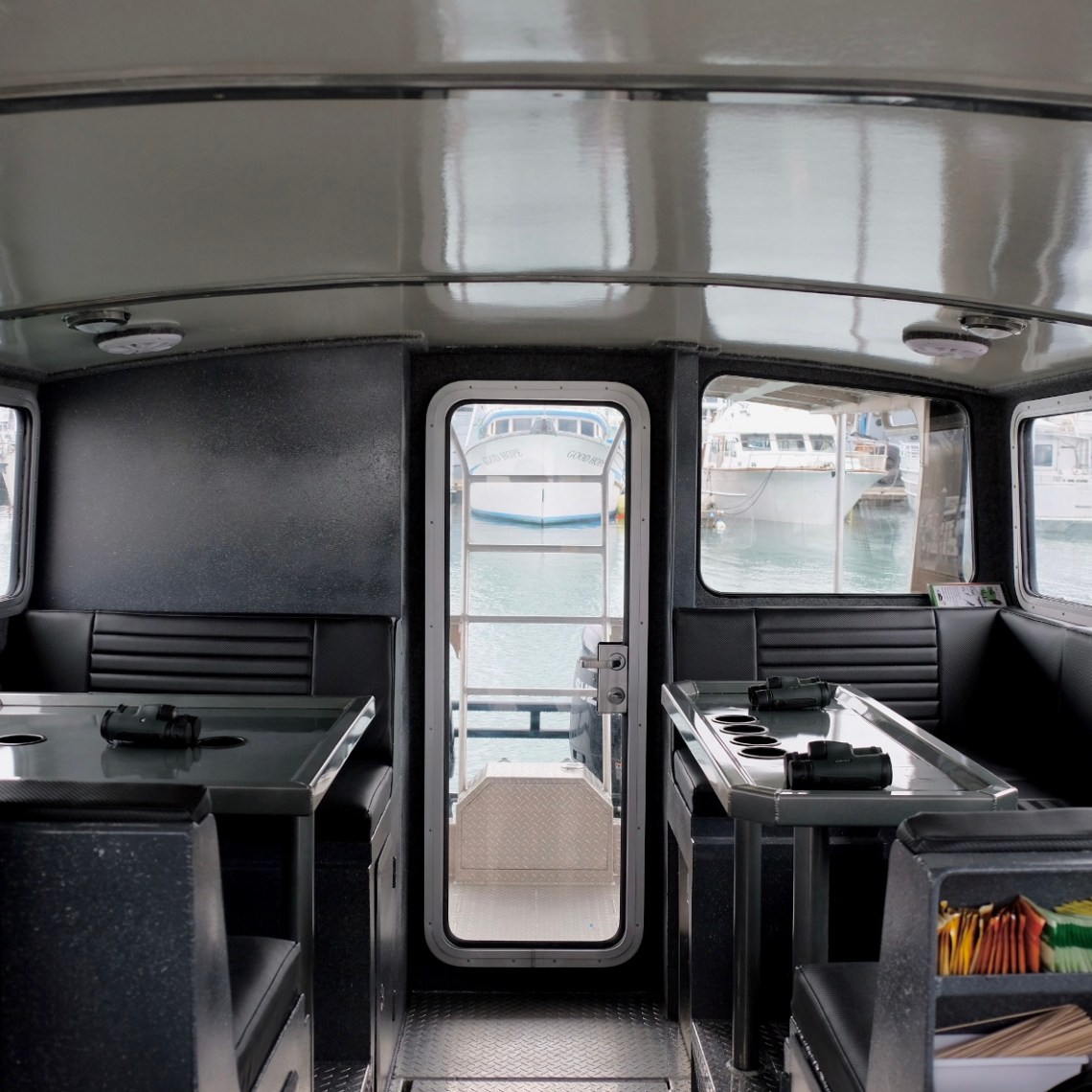 Interior of a boat cabin with tables, seats, and a central door leading outside.
