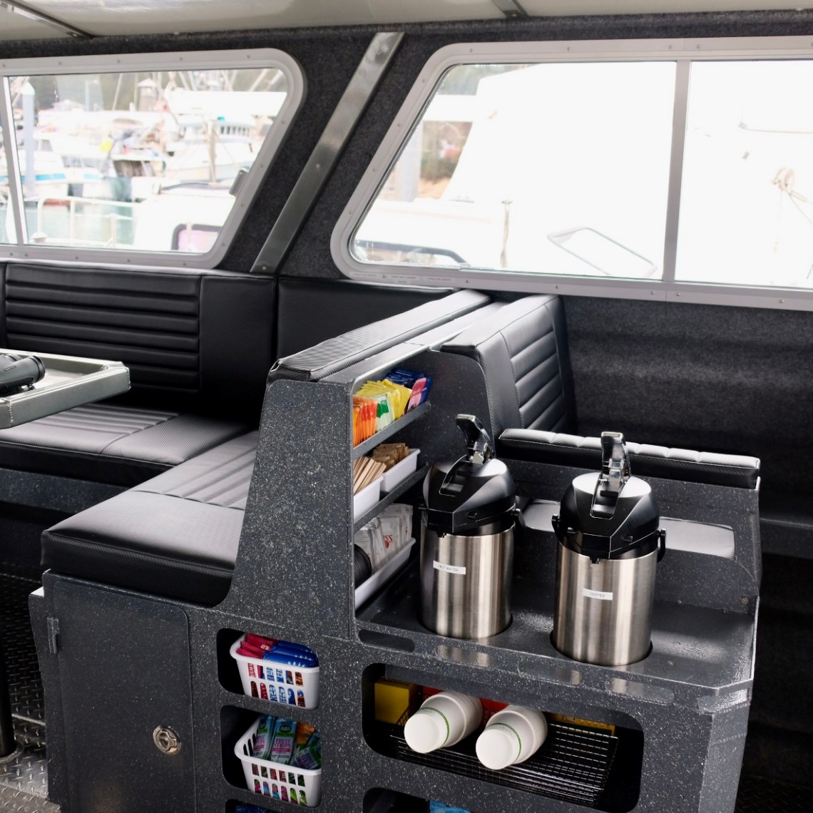 Interior of a boat with seating, tables, and beverage dispensers.