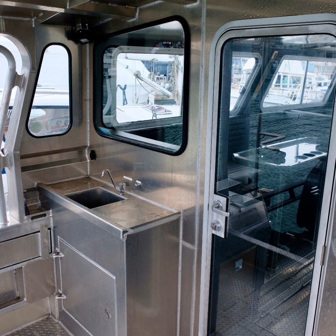 Stainless steel boat cabin kitchen with sink and glass door.