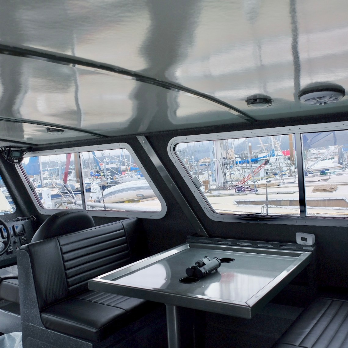 Interior of a boat with seating, table, and marina view outside windows.